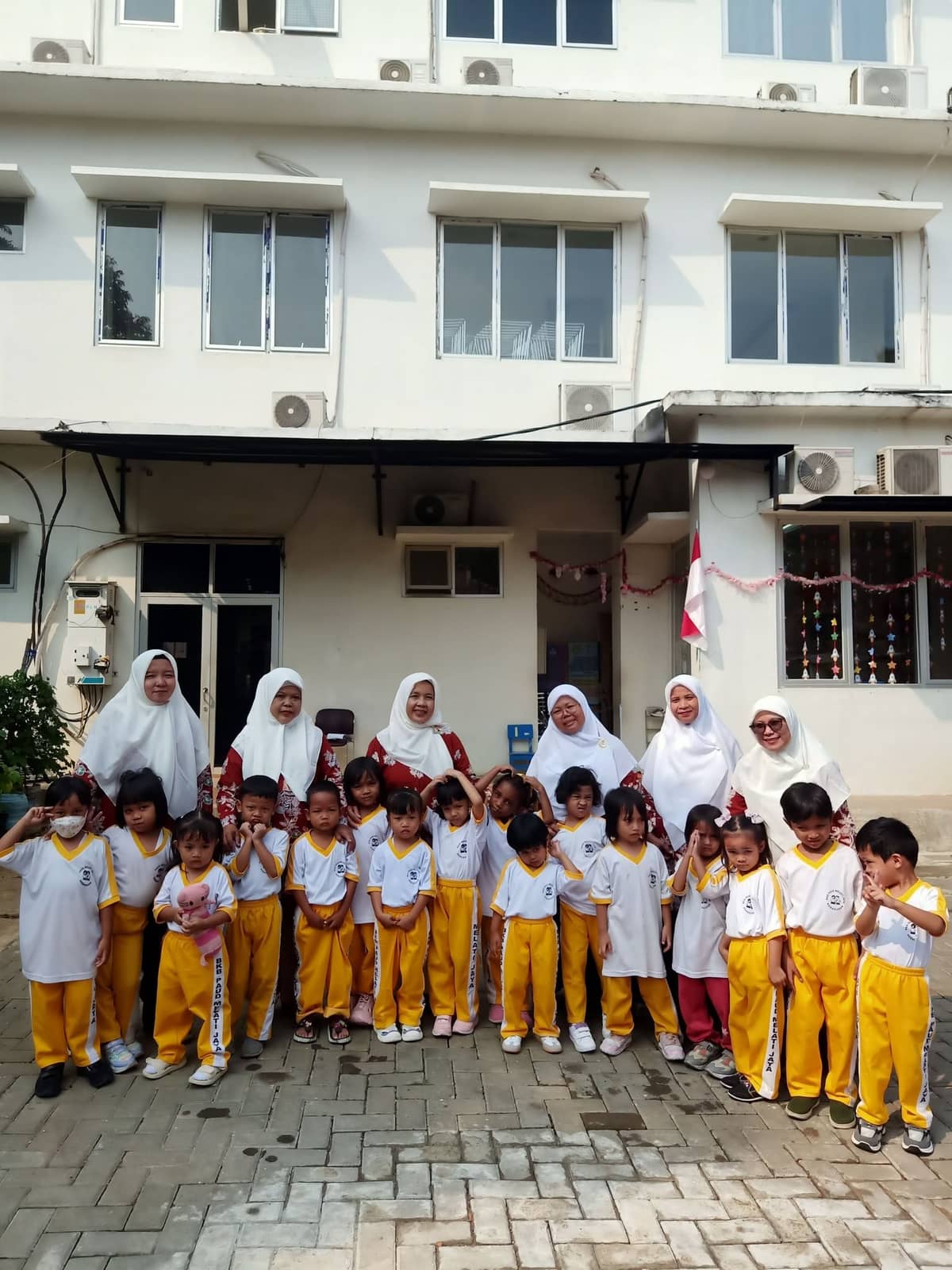 Guru berfoto bersama anak-anak berseragam di halaman sekolah